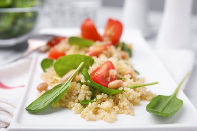 Photo of Delicious quinoa salad with tomatoes, beans and spinach leaves served on table, closeup