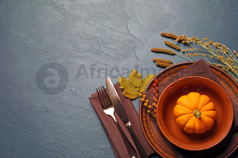 Autumn table setting with floral decor and pumpkin on dark grey background, flat lay. Space for text