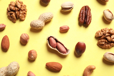 Different delicious nuts on yellow background, flat lay
