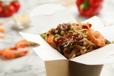 Box of wok noodles with seafood on light  table, closeup