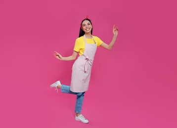 Young housewife wearing apron on pink background