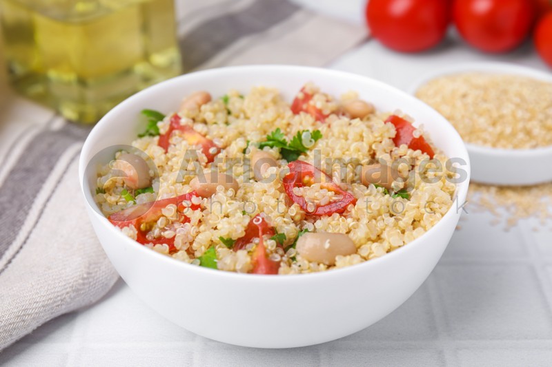 Delicious quinoa salad with tomatoes, beans and parsley served on white tiled table
