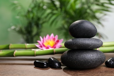 Stacked spa stones, bamboo stems and flower on wooden table against blurred background. Space for text