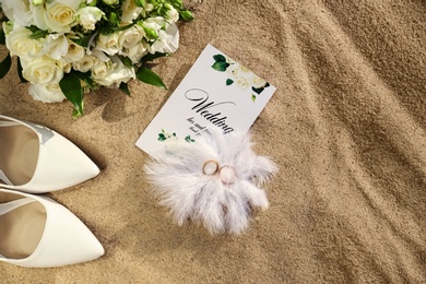 Flat lay composition with wedding invitation and gold rings on sandy beach