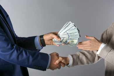 Man shaking hands with woman and offering bribe on grey background, closeup