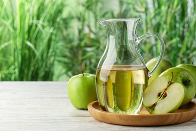 Jug of tasty juice and fresh ripe green apples on white wooden table outdoors, space for text