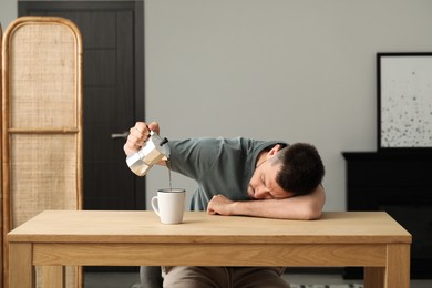 Photo of Sleepy man pouring coffee in cup at wooden table indoors