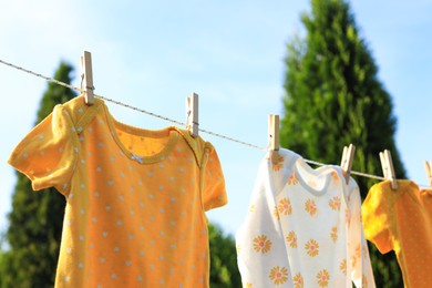 Clean baby onesies hanging on washing line in garden. Drying clothes