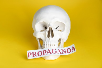 Photo of Information warfare concept. Human skull and paper card with word Propaganda on yellow background