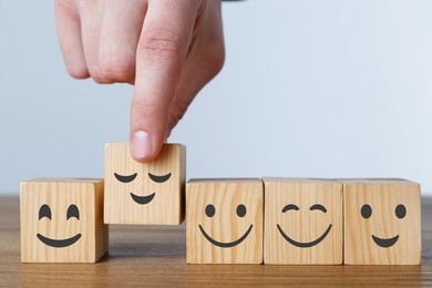 Image of Man arranging cubes with different emoticons in row on wooden table against light background, closeup