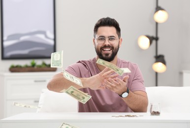 Happy young man throwing money at white table indoors