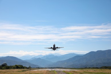 Modern white airplane landing on runway near mountains