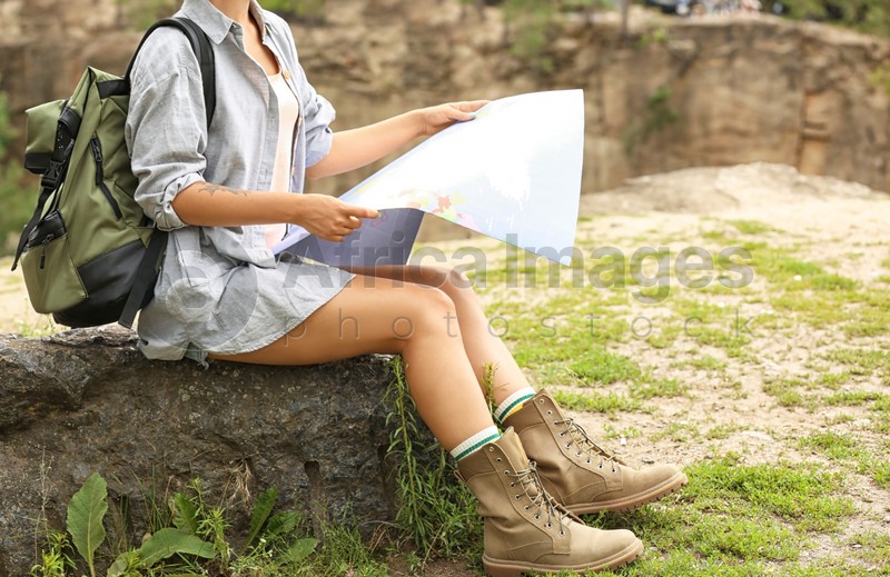 Young woman with map sitting on rock in forest. Camping season