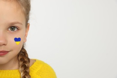 Little girl with drawing of Ukrainian flag on face in heart shape against white background, closeup. Space for text