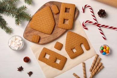 Parts of gingerbread house, ingredients and fir tree branch on white wooden table, flat lay
