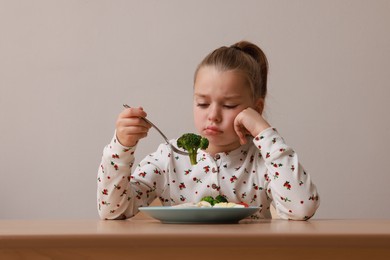 Cute little girl refusing to eat her dinner at table on grey background