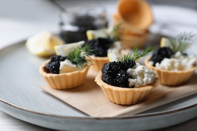 Photo of Delicious tartlets with black caviar, cream cheese and lemon served on light table, closeup