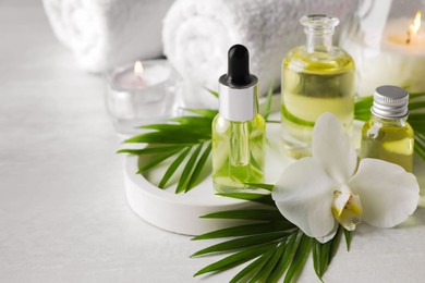 Photo of Essential oils, orchid flower and green leaves on white table, closeup