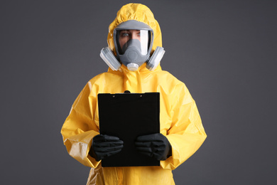 Woman in chemical protective suit holding clipboard on grey background. Virus research