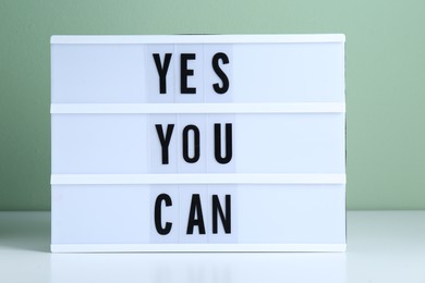 Lightbox with phrase Yes You Can on table against light green background. Motivational quote