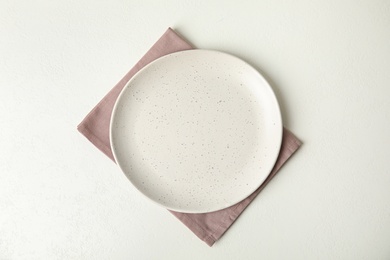 Empty plate and napkin on white table, top view