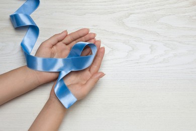 Photo of Woman holding light blue awareness ribbon at white wooden table, top view. Space for text
