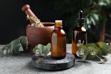 Photo of Bottles of eucalyptus essential oil, leaves and mortar on light grey table