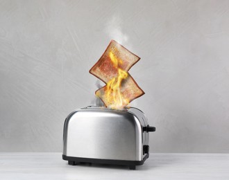 Toaster flaming up while cooking slices of bread on white wooden table. Unsafe appliance 