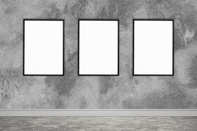 Frames with empty canvases on grey wall in modern art gallery. Space for design