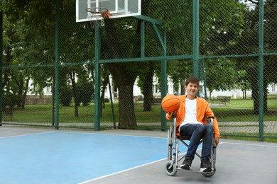 Disabled teenage boy in wheelchair with basketball ball at outdoor court