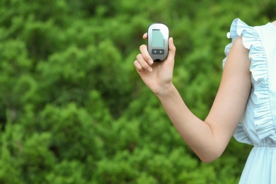 Woman holding digital glucometer on blurred background. Diabetes control