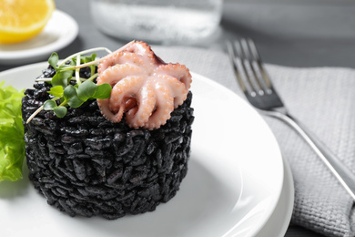 Photo of Delicious black risotto with baby octopus on table, closeup