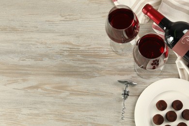 Glasses and bottle of red wine with chocolate candies on white wooden table, flat lay. Space for text