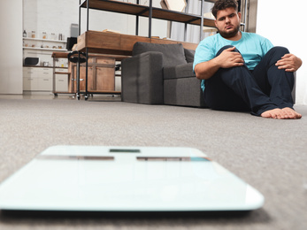 Depressed overweight man looking at scales in living room