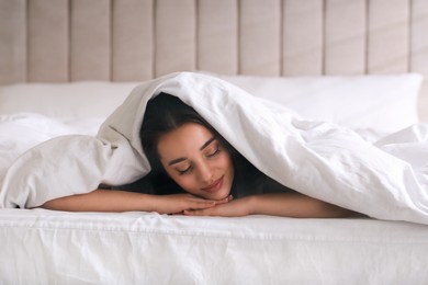 Young woman covered with warm white blanket sleeping in bed