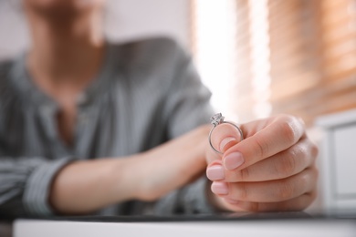 Woman holding wedding ring at table indoors, space for text. Divorce concept