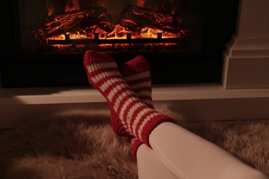 Photo of Woman in warm socks resting near fireplace with burning woods indoors, closeup