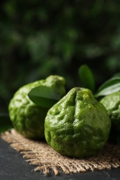 Photo of Fresh ripe bergamot fruits with green leaves on black table against blurred background