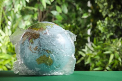 Photo of Globe in plastic bag on table against green leaves, space for text. Environmental conservation