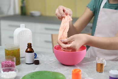 Little girl kneading DIY slime toy at table in kitchen, closeup