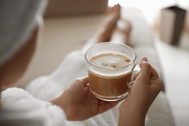 Woman with cup of hot drink on sofa at home in morning, closeup