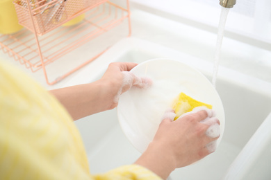 Woman washing ceramic plate in kitchen, closeup