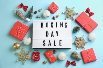 Lightbox with phrase BOXING DAY SALE and Christmas decorations on light blue background, flat lay