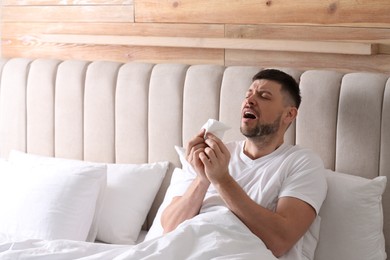 Man suffering from runny nose in bed. Space for text