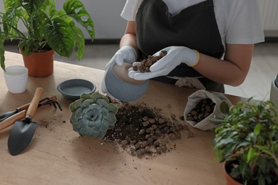 Woman filling flowerpot with drainage at table indoors, closeup. Transplanting houseplant