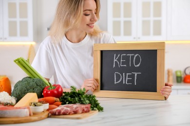 Woman holding blackboard with phrase Keto Diet at white table in kitchen, closeup