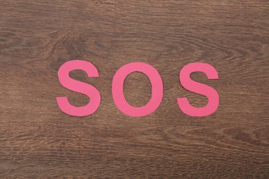 Abbreviation SOS made of paper letters on wooden background, top view