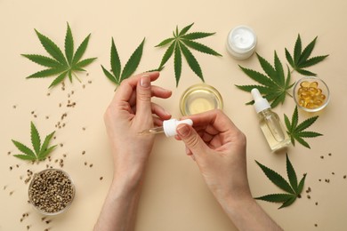 Woman applying CBD oil or THC tincture on skin at beige background, top view