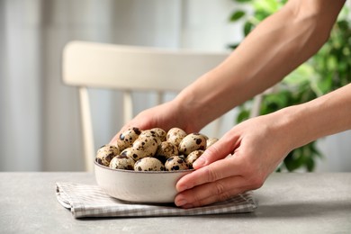Woman with bowl of quail eggs at table indoors, closeup