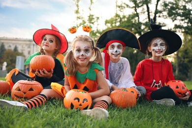 Photo of Cute little kids with pumpkins wearing Halloween costumes in park